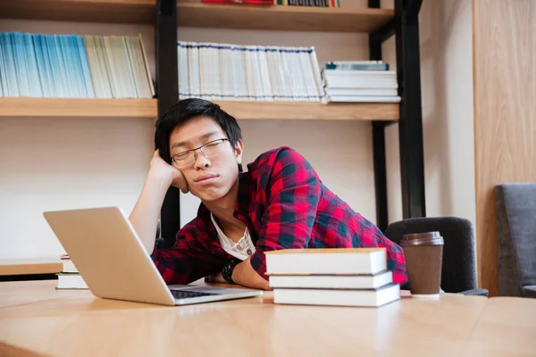 Hombre durmiendo en la biblioteca cerca de la computadora portátil y libros —  Fotos de Stock