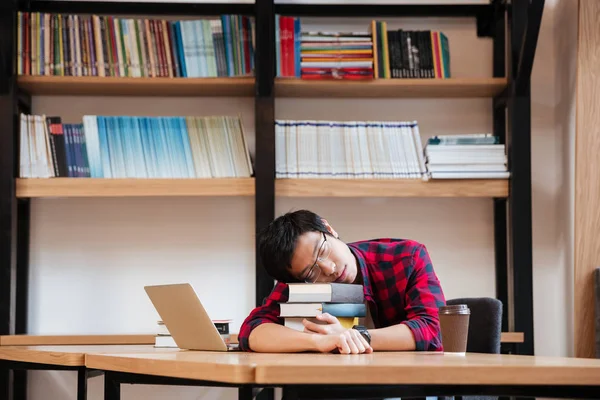 Ung man sover på böcker på biblioteket nära laptop — Stockfoto