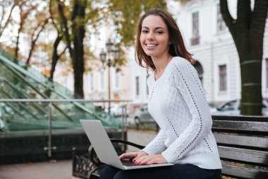 Oturma ve parkta bankta dizüstü kullanarak neşeli kadın
