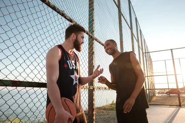 Happy tersenyum pemain basket berbicara saat berdiri di taman bermain — Stok Foto