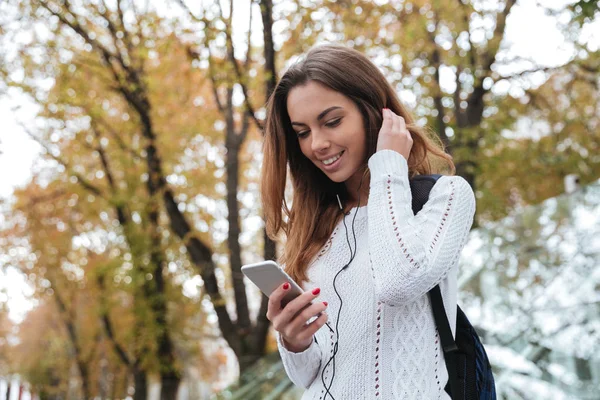 Mosolygó csinos, fiatal nő, hallgató-hoz zene-ból smartphone kint — Stock Fotó