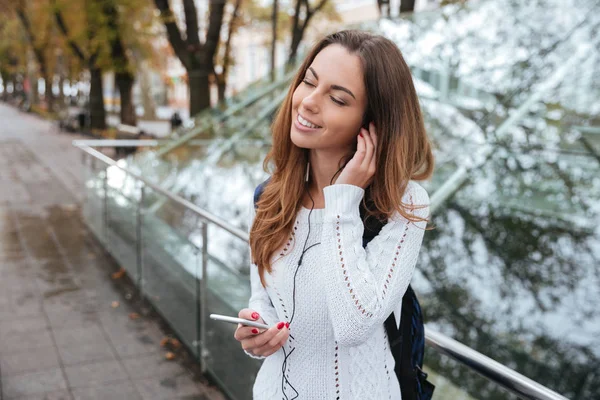 Mujer sonriente escuchando música desde el teléfono celular en el parque —  Fotos de Stock