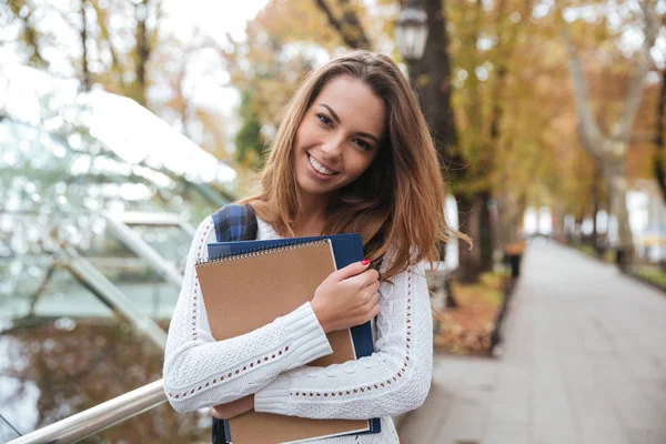 Uśmiechnięta kobieta z notebookami, stojąc w parku — Zdjęcie stockowe