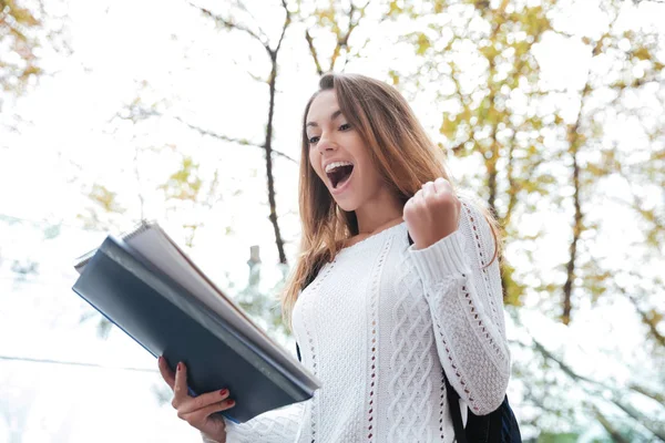 Χαρούμενα γυναίκα ενθουσιασμένος με σημειωματάριο φωνάζοντας και γιορτάζει την επιτυχία — Φωτογραφία Αρχείου