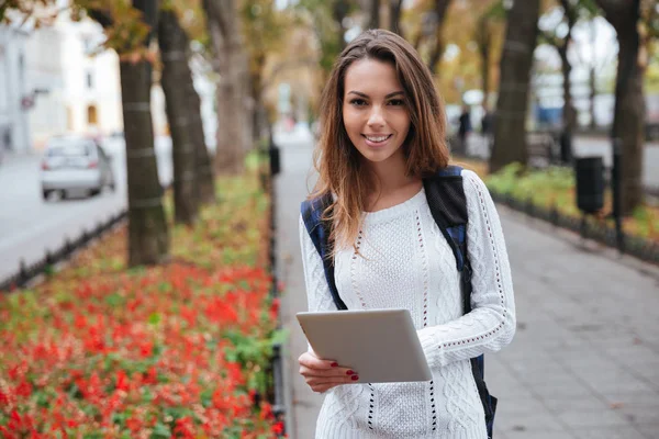Gülümseyen sevimli genç kadın parkta tablet kullanma sırt çantası ile — Stok fotoğraf