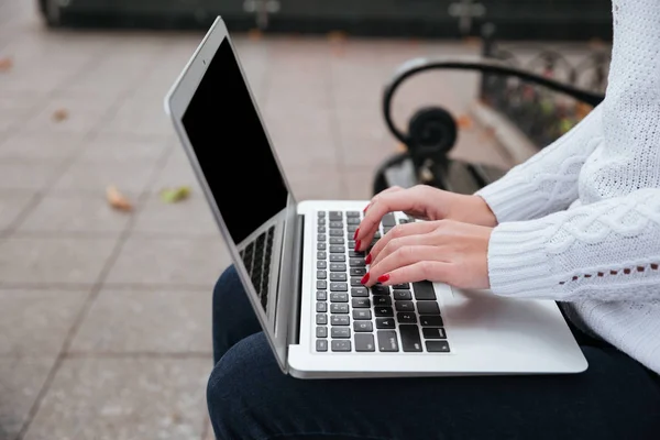 Laptop usado por mãos de mulher jovem sentado no banco ao ar livre — Fotografia de Stock