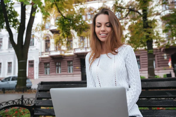 Mujer alegre sonriendo y utilizando el ordenador portátil en el parque —  Fotos de Stock