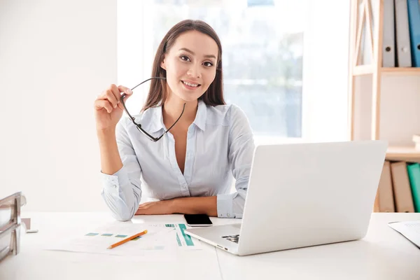 Empresaria sosteniendo gafas sentada y usando laptop — Foto de Stock