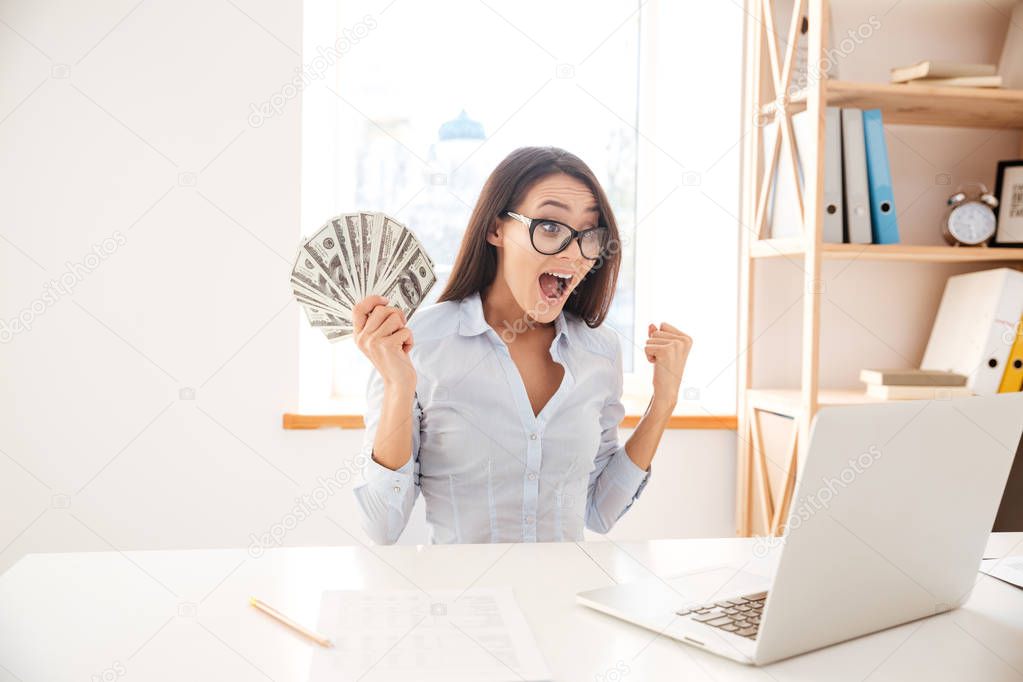 Businesswoman holding money in hand while making winner gesture