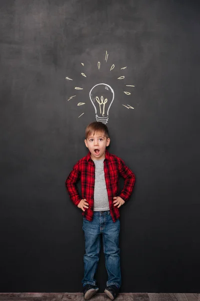 Little surprised boy having idea over chalkboard background with drawings