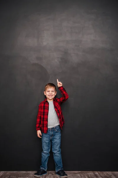 Gelukkige jongen boven schoolbord staan en die omhoog wijst — Stockfoto
