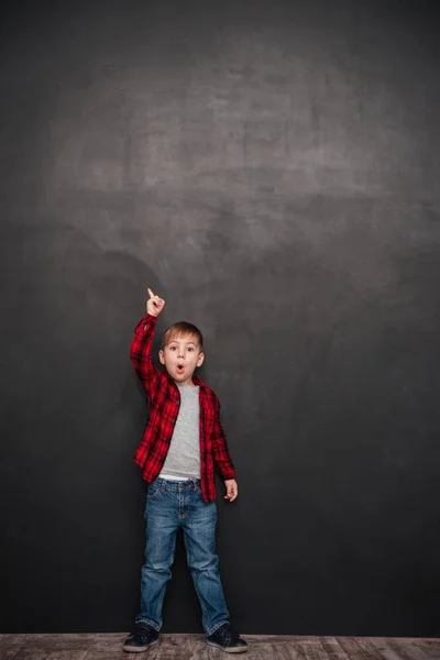Geschokt jongetje boven schoolbord staan en die omhoog wijst — Stockfoto