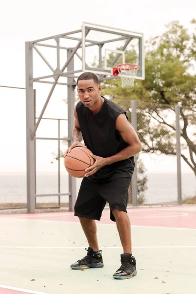 Jovem jogador de basquete feliz sentado no parque com uma toalha