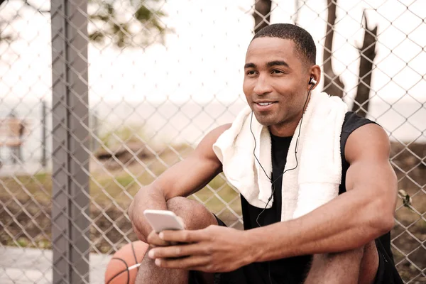 Jogador de basquete sentado no parque com telefone e ouvir música — Fotografia de Stock