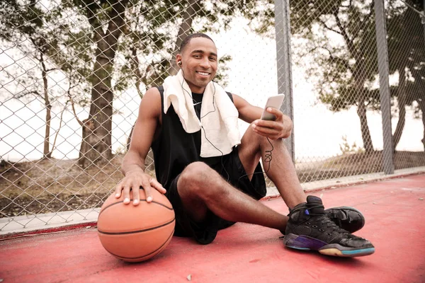 Jugador de baloncesto africano alegre sentado con toalla mientras lista — Foto de Stock