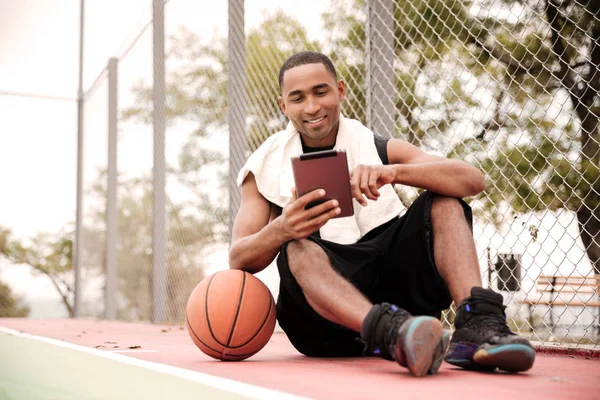 Jogador de basquete africano feliz sentado no parque e usando tablet — Fotografia de Stock