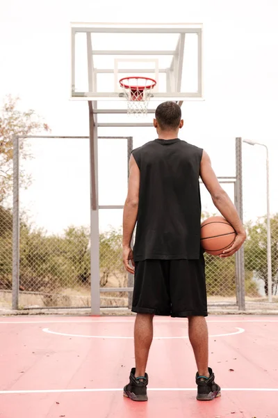 Visão traseira do jogador de basquete de pé e segurando bola — Fotografia de Stock