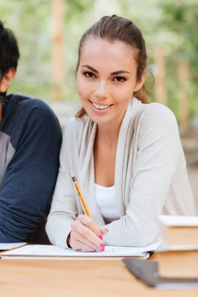 Lachende aantrekkelijke jonge vrouw zitten en schrijven — Stockfoto