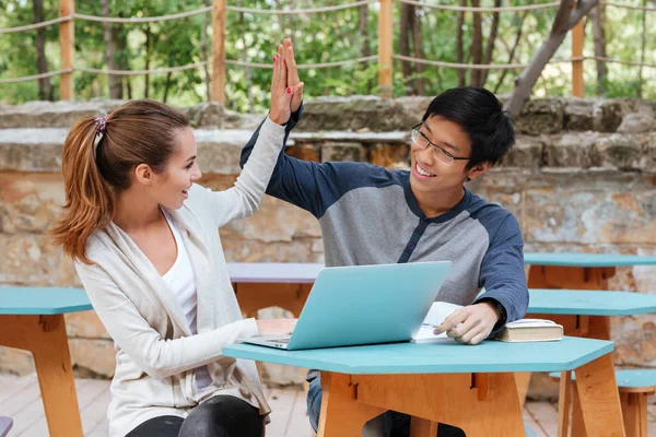 Succesvolle paar met behulp van de laptop en het geven van hoge vijf buitenshuis — Stockfoto