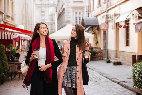 Dos mujeres sonrientes caminando y tomando café en el casco antiguo —  Fotos de Stock