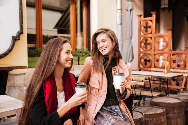 Две веселые женщины с чашками кофе разговаривают и смеются — стоковое фото