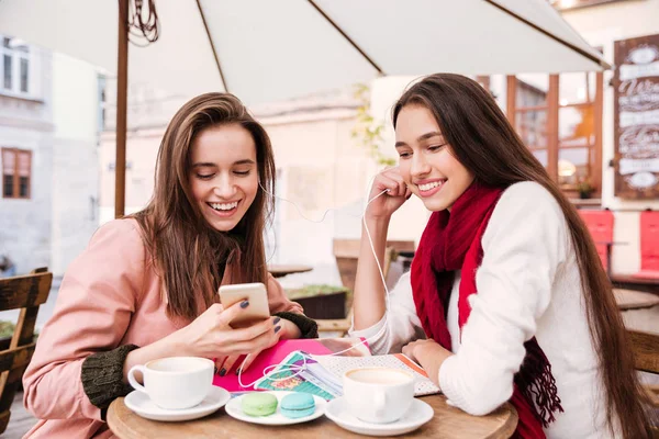 Poslech hudby ze smartphonu ve venkovní kavárně dvě ženy — Stock fotografie