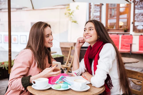 Two women listening to music with earphones in outdoor cafe — Stock Photo, Image