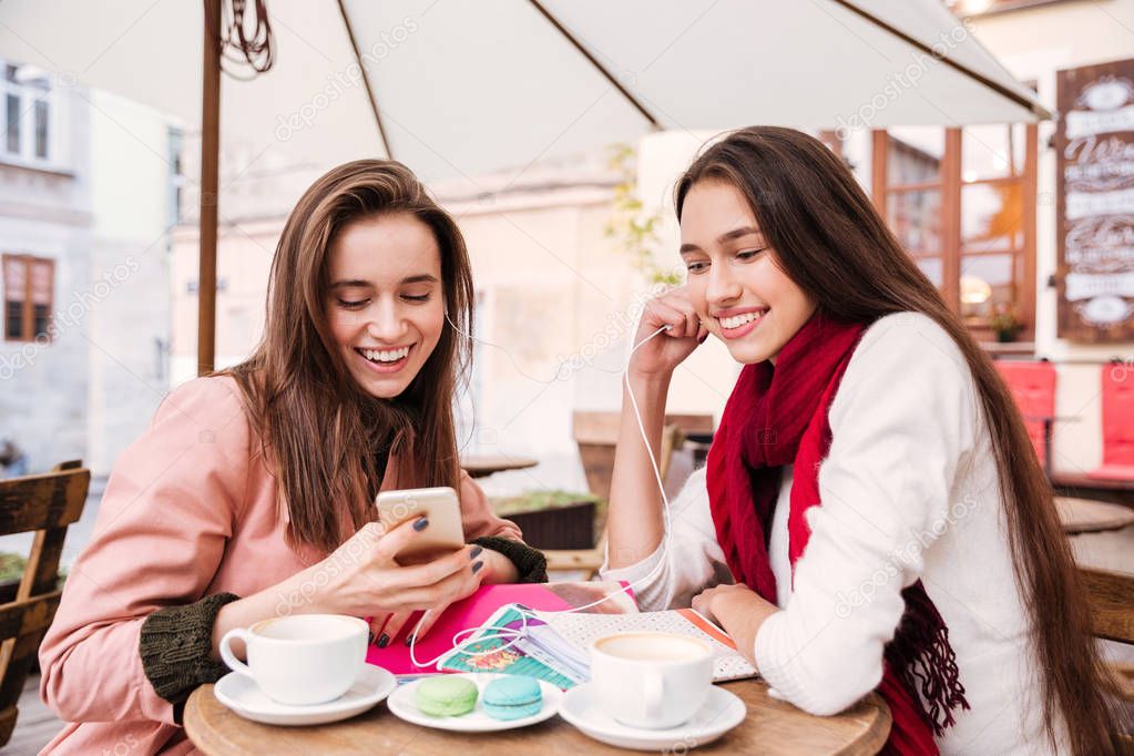 Two women listening to music from smartphone in outdoor cafe