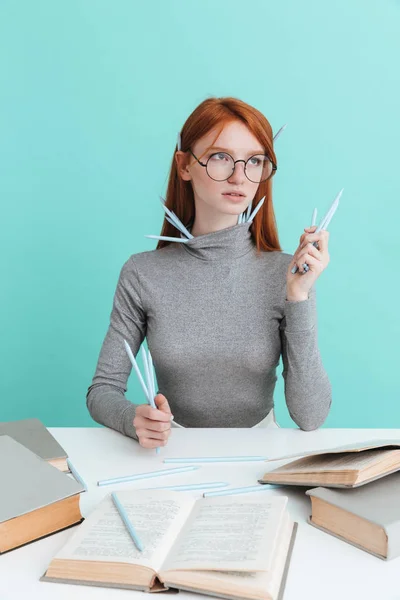 Jolie femme en lunettes rondes avec des crayons assis et lisant — Photo