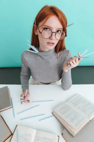 Attraktive rothaarige junge Frau mit Bleistiften sitzen und lesen — Stockfoto