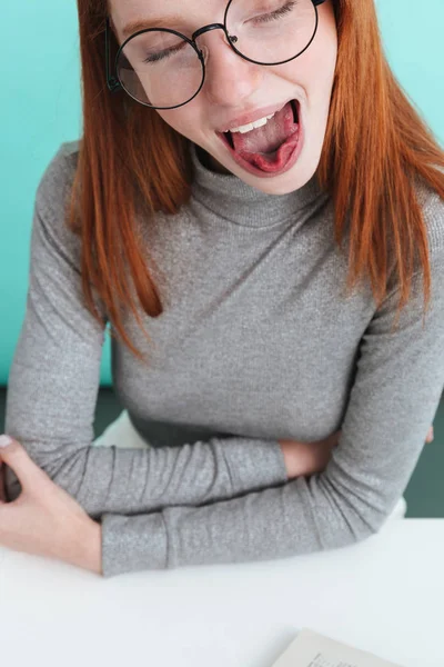 Mujer joven divertida en gafas redondas sentado y mostrando la lengua — Foto de Stock