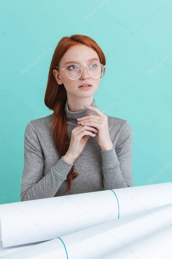 Thoughtful beautiful young woman sitting at the table with blueprints
