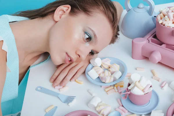Tired woman lying on table with plasic tableware and marshmallows — Stock Photo, Image