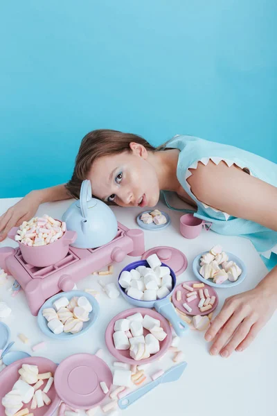 Utmattad kvinna liggande på bordet med plasic rätter och marshmallows — Stockfoto