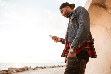 Sahilde yürüyüş ve müzik dinleme sırasında chat yapan adam