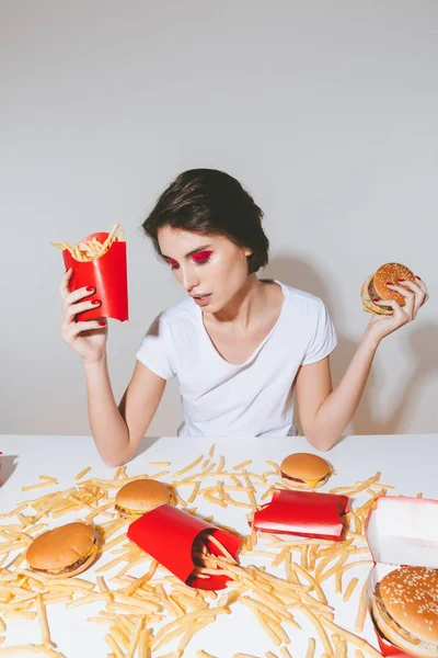 Bonita joven sosteniendo papas fritas y hamburguesa — Foto de Stock