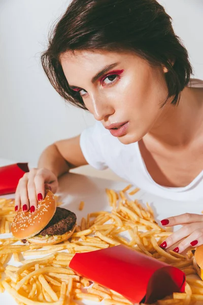 Mujer sentada a la mesa con hamburguesa y papas fritas —  Fotos de Stock