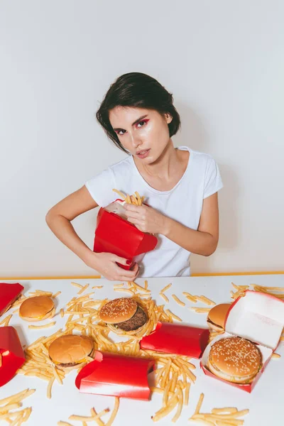 Γοητευτική γυναίκα κάθεται και τρώγοντας τηγανητές πατάτες από το κόκκινο κουτί — Φωτογραφία Αρχείου
