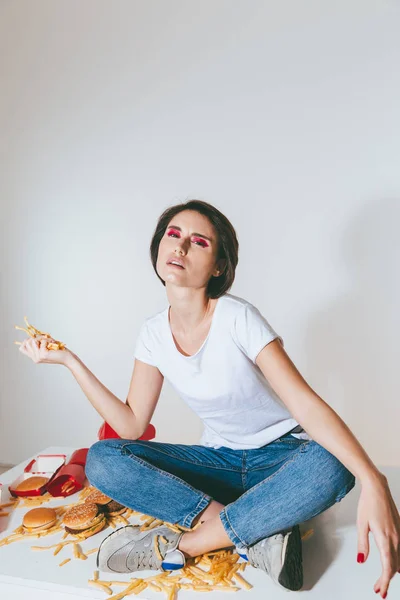 Mujer sentada en la mesa y sosteniendo papas fritas — Foto de Stock