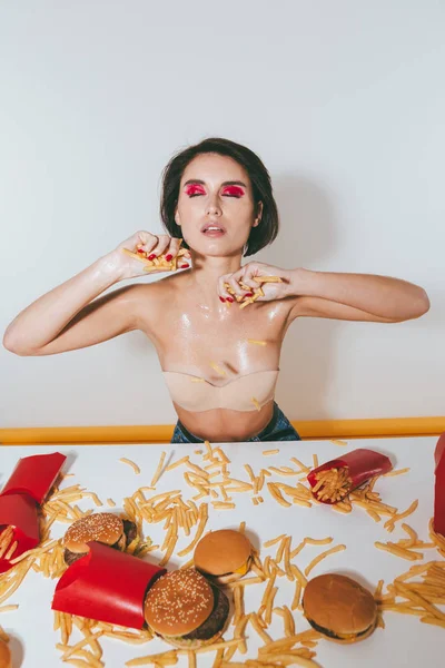 Jovem sedutora segurando batatas fritas na mesa — Fotografia de Stock