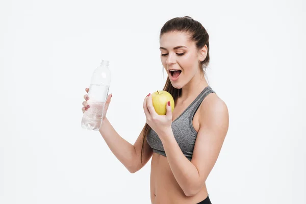 Mladý sportovní láhev s vodou žena hospodářství a kousání apple — Stock fotografie