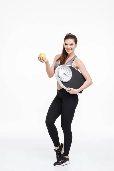 Feliz mujer de fitness sonriente de pie, sosteniendo una manzana y escamas — Foto de Stock