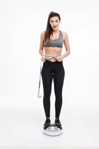 Fitness woman standing on scales and holding tape measue — Stock Photo, Image