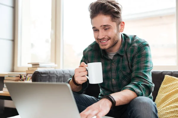 Glücklicher Mann schaut auf Laptop auf Sofa — Stockfoto