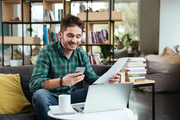 Lykkelig mann med dokumenter sittende på sofaen ved bordet – stockfoto