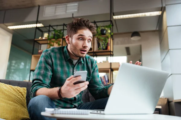 Hombre sorprendido con teléfono y portátil — Foto de Stock