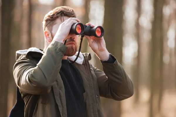 Serious bearded man looking at field-glass in the forest. — Stock Photo, Image