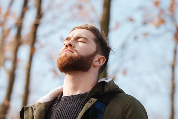 Homem barbudo relaxado em pé na floresta com os olhos fechados . — Fotografia de Stock