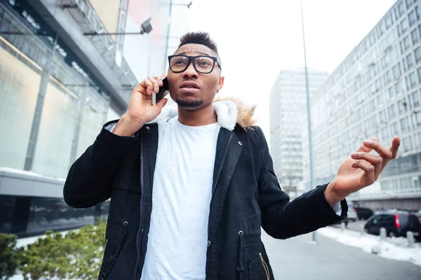 Förvirrad afrikanska man går på gatan när du talar genom mobiltelefon — Stockfoto