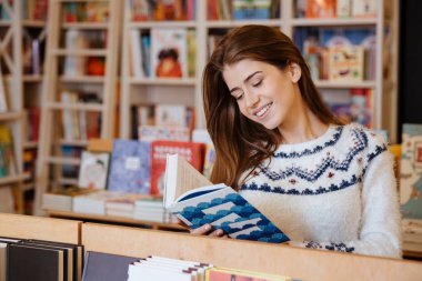 Genç güzel kadın ayakta ve kitaplığındaki kitap okuma